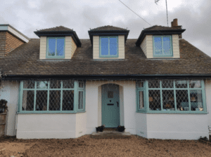 Two light green uPVC splay bay windows on the right and left side of a cottage.