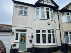 A cream coloured home fitted with two white uPVC circular bay windows on the ground and first floor. The house also has a white casement window and a light green composite door.